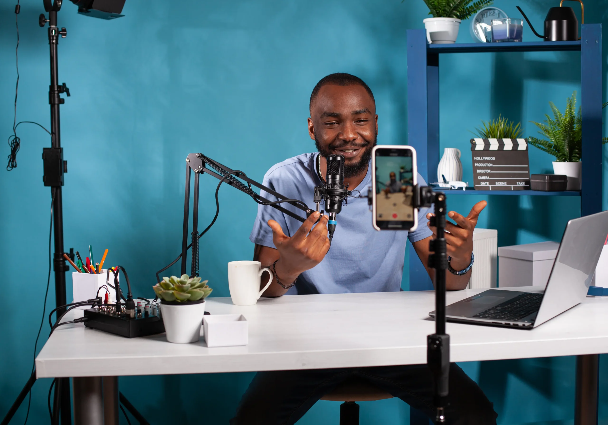 content-creator-interacting-with-fanbase-studio-looking-live-video-podcast-setup-sitting-desk-smiling-vlogger-talking-with-audience-front-recording-smartphone-online-live-show